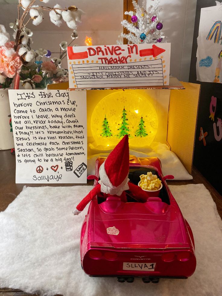 a red toy car with a santa clause hat on it's head in front of a christmas display