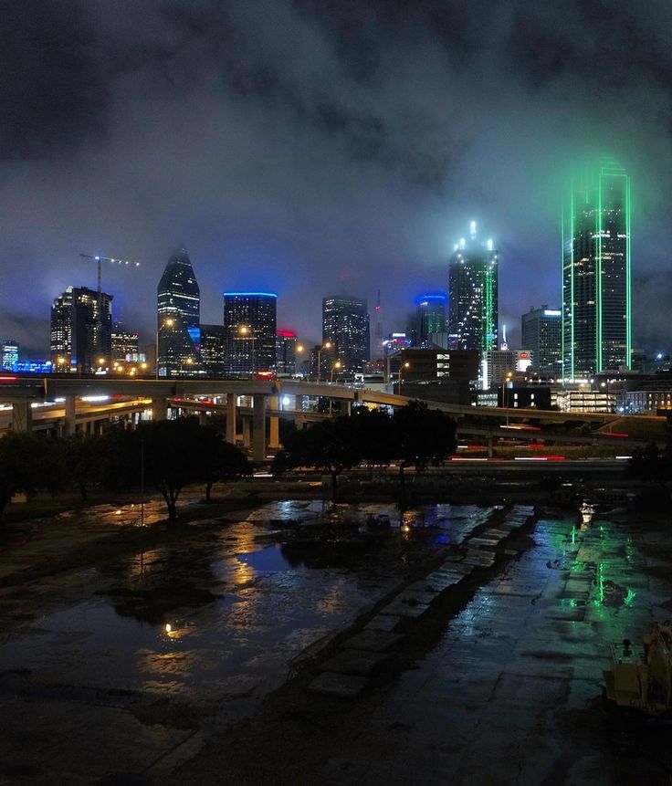 the city skyline is lit up in green and blue as rain falls on the ground