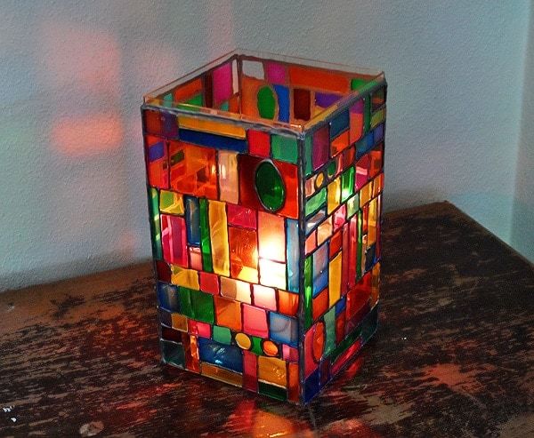 a multicolored candle holder sitting on top of a wooden table next to a wall