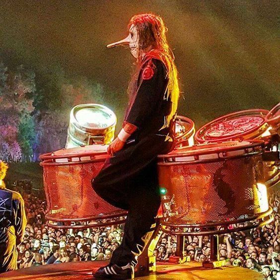 a man with long hair sitting on top of a drum set in front of a crowd