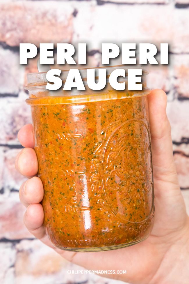 a hand holding a mason jar filled with orange colored sauce and garnished with herbs