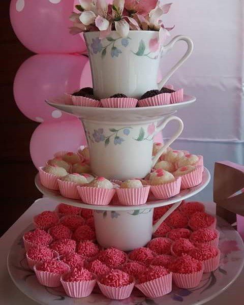 three tiered cake stand with cupcakes and tea cups on it, decorated with pink flowers