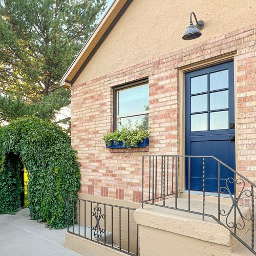 a brick building with a blue door and black iron handrails on the front steps