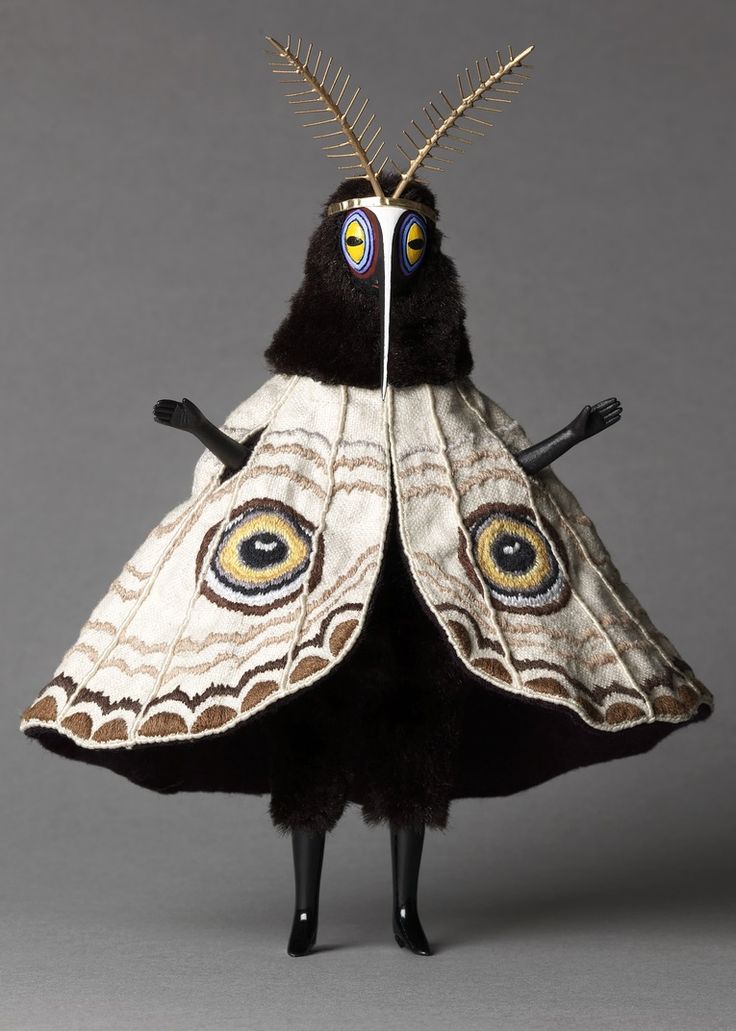 a stuffed animal wearing a white and black dress with large eyes on it's wings