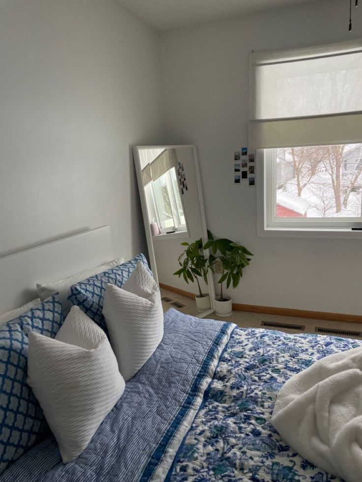 a bed with blue and white comforter in a bedroom next to a large window