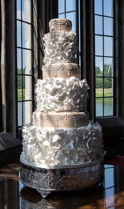 a wedding cake sitting on top of a table in front of large windows with the bride and groom's name written on it