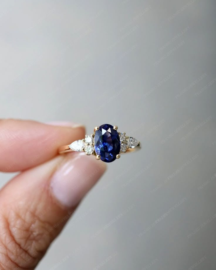 a woman's hand holding an engagement ring with a blue sapphire and diamond accents