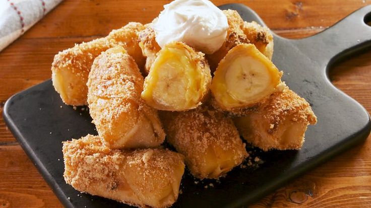 some bananas and whipped cream are on a black plate with a knife next to it