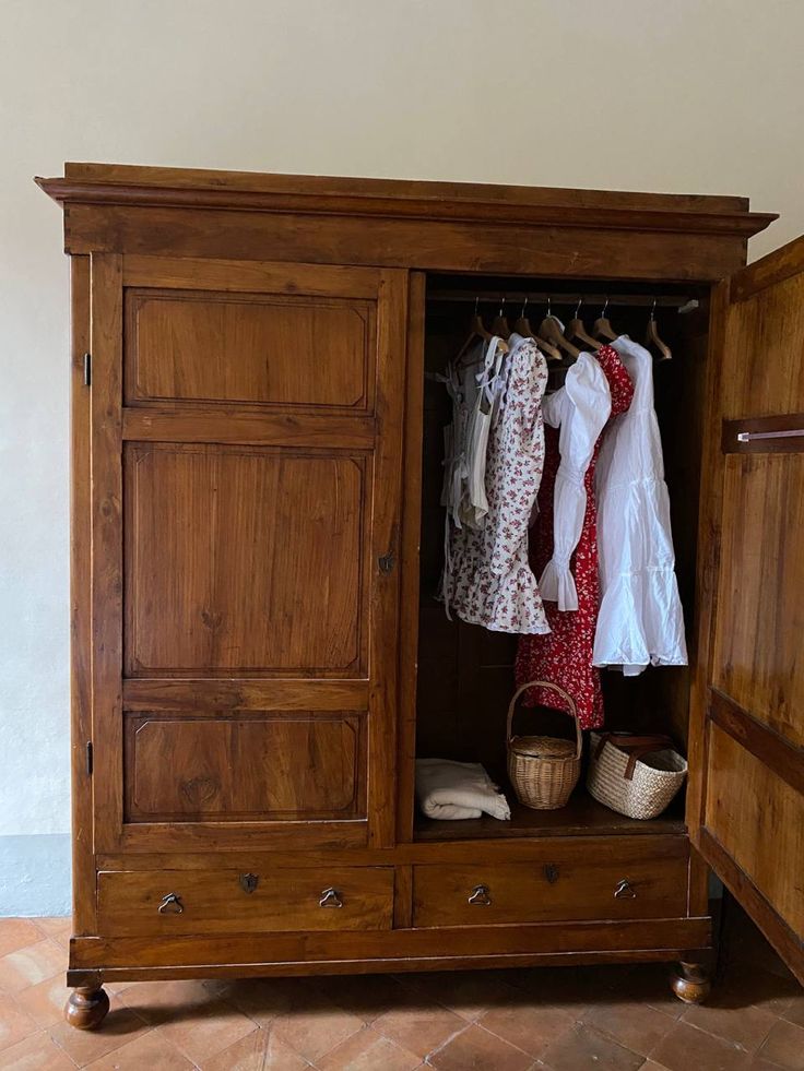 an old wooden armoire with clothes hanging on it