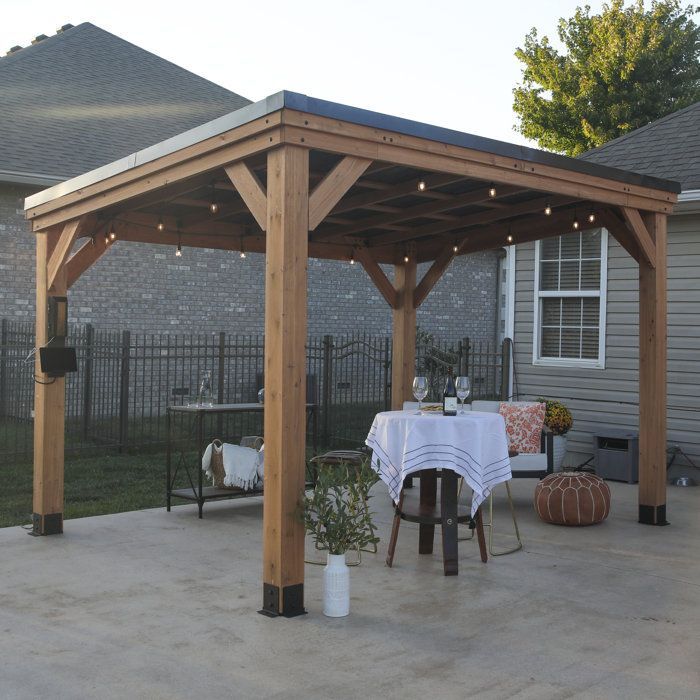 a patio with a table and chairs under a wooden gazebo covered in string lights