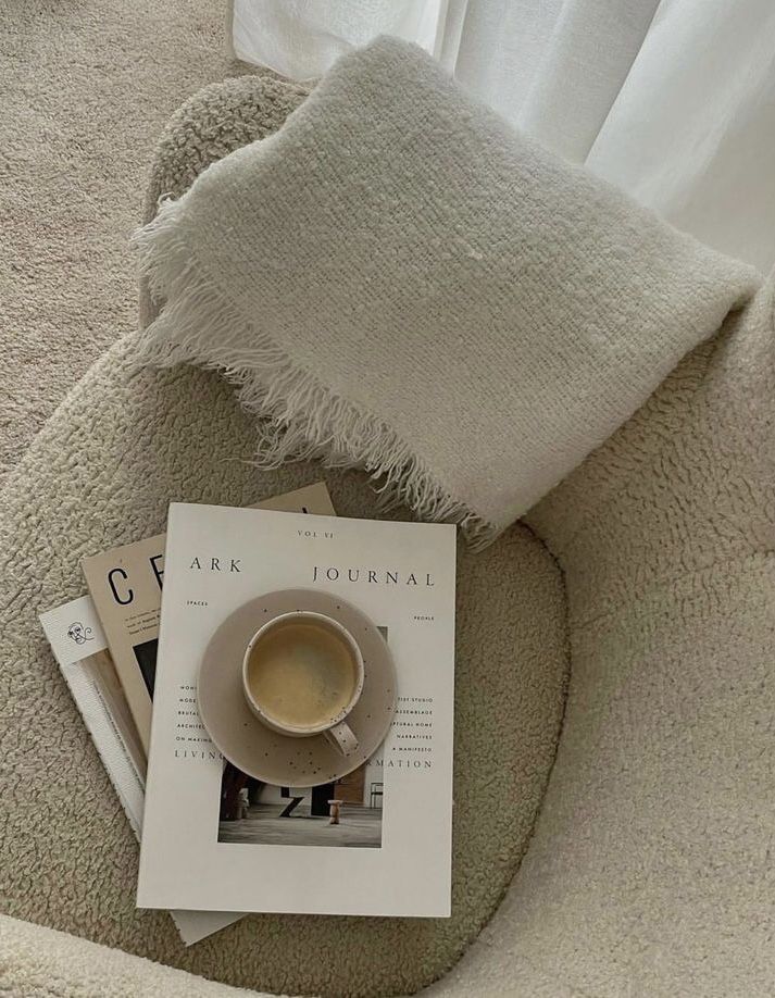 a cup of coffee sitting on top of a white chair next to a book and some magazines