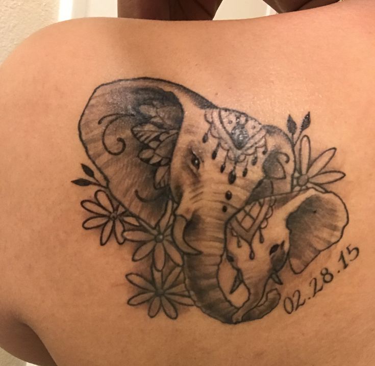 an elephant tattoo on the back of a woman's upper body, with flowers around it