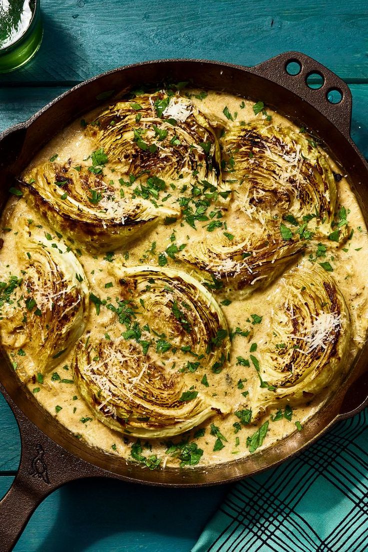 an iron skillet filled with artichokes covered in yellow sauce and garnished with parsley