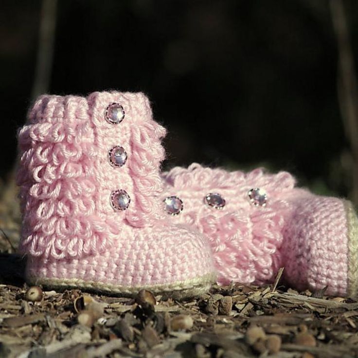 a pair of pink crocheted baby boots sitting on the ground with rocks around them