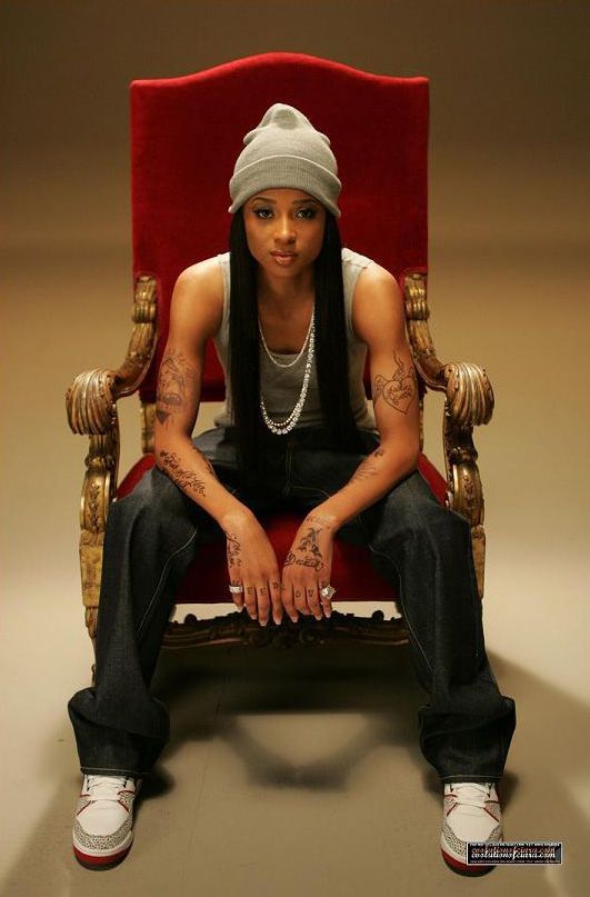 a woman sitting on top of a red chair in front of a white wall and wearing a beanie