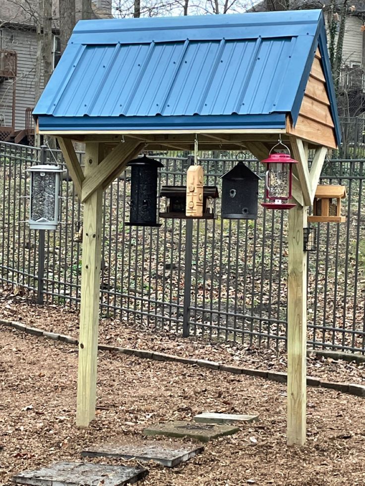 a blue roofed bird house in the middle of a fenced area with birds hanging from it