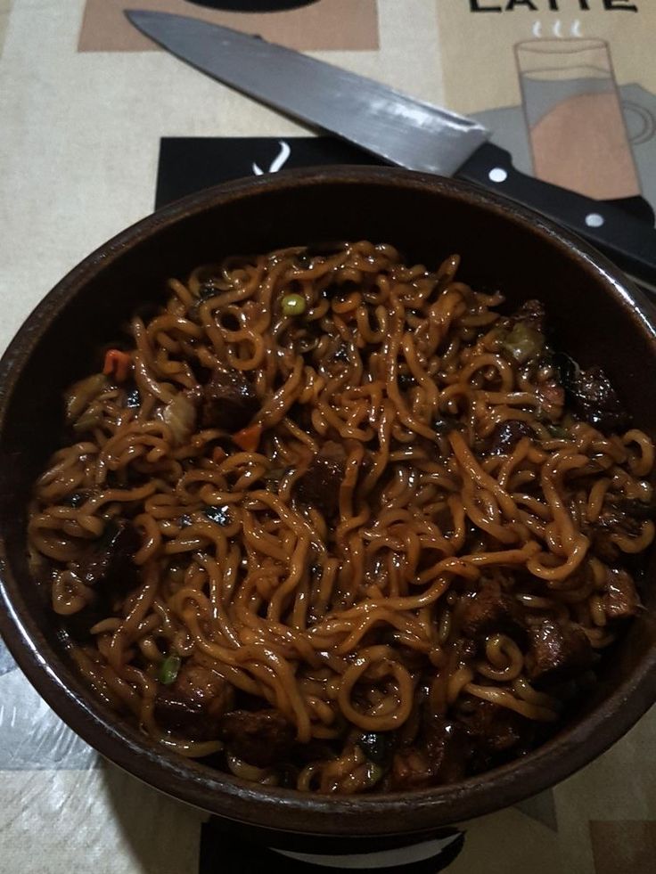 a bowl filled with noodles and meat sitting on top of a table next to a knife