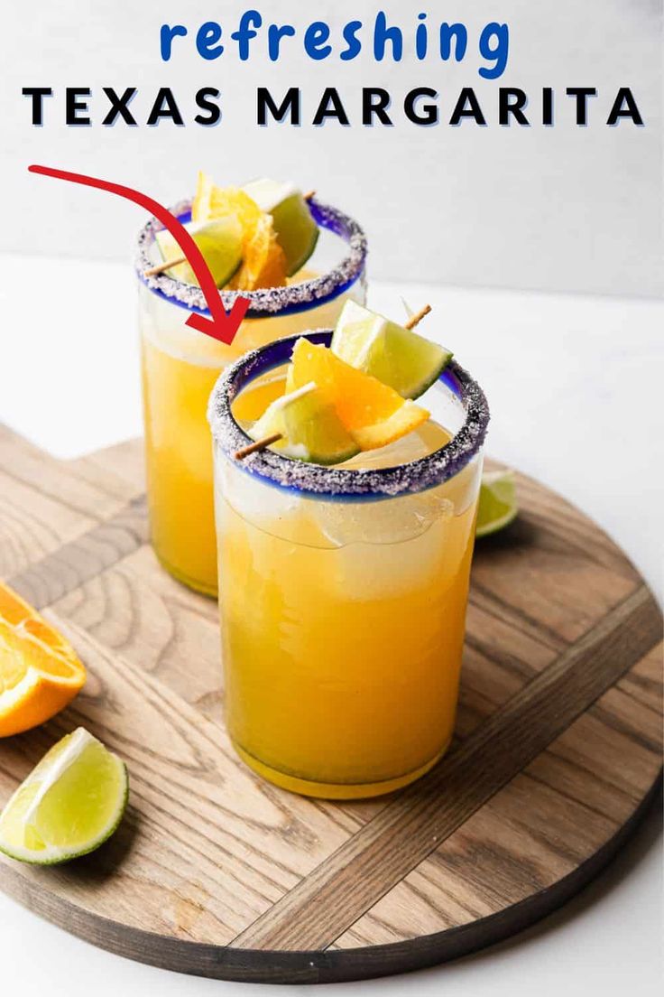 two glasses filled with orange margaritas on top of a cutting board