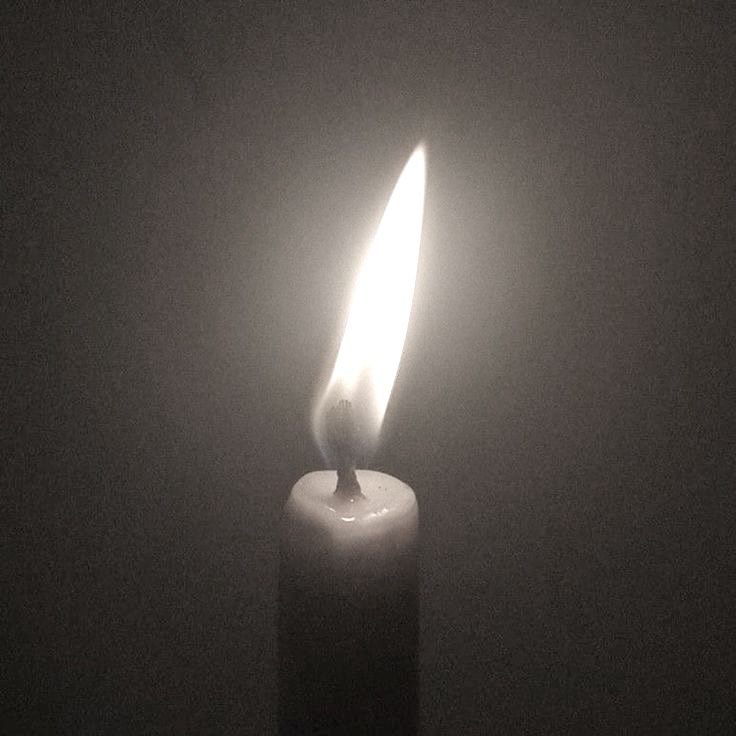 a lit candle in the dark with only one light shining on it's side