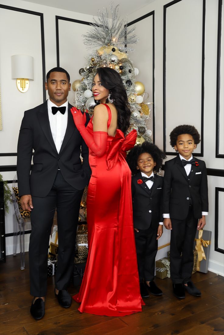 a man and woman in formal wear standing next to a christmas tree with two children