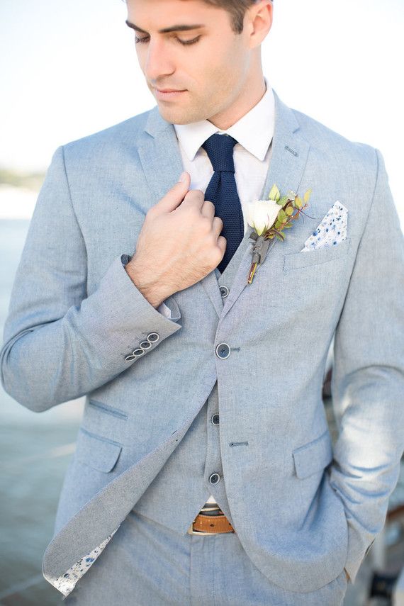 a man in a gray suit and blue tie is tying his boutonniere