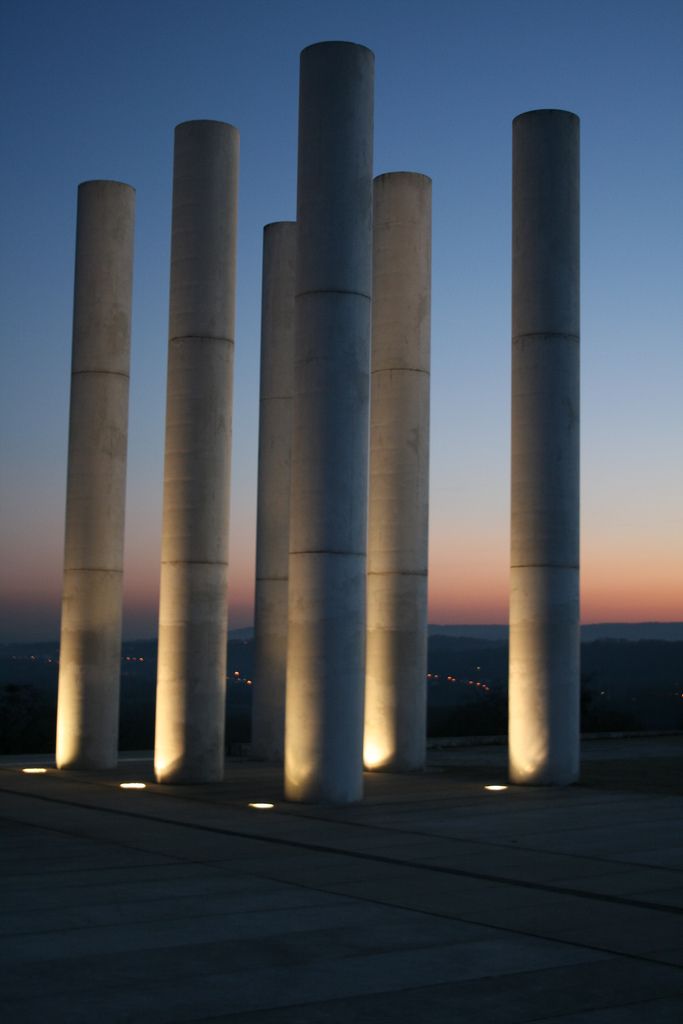 four cement pillars are lit up at night with the sky in the background and lights behind them