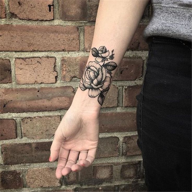 a woman's arm with a flower tattoo on her left hand and a brick wall in the background