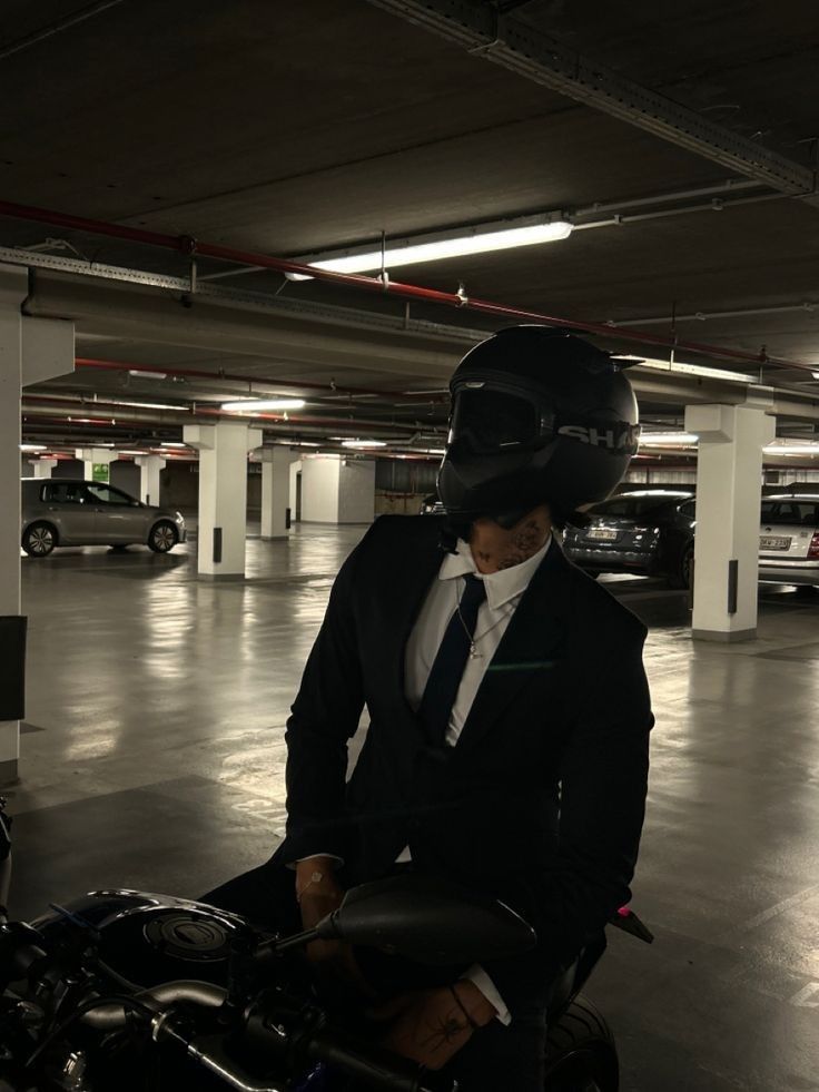 a man wearing a suit and tie standing next to a motorcycle in a parking garage