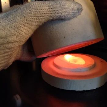 a person holding a lit candle in front of an object that is on top of a table