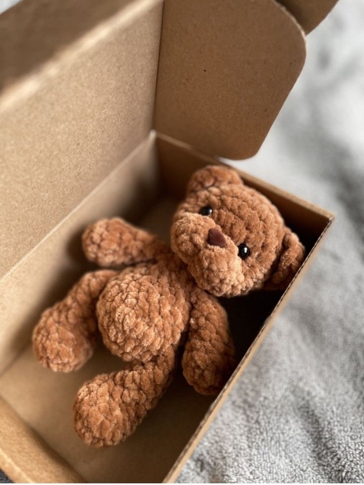 a brown teddy bear sitting inside of a cardboard box