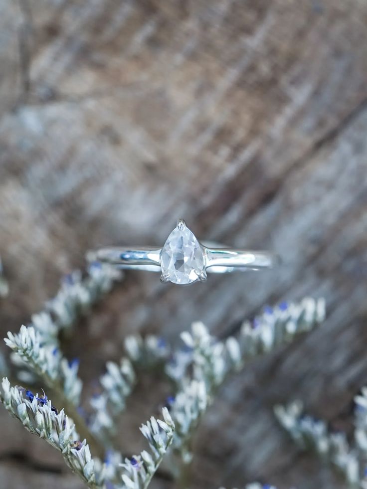 Highlighting a clear white pear-shaped gemstone delicately cradled in a basket prong setting.This pear topaz ring can also serve as a placeholder ring or stand-in ring, embodying the anticipation and excitement of what the future holds. Topaz is the November birthstone. Each piece of our jewelry is handcrafted with love. White Pear Shaped Ring With Rose Cut Diamonds, Diamond White Solitaire Teardrop Ring, Teardrop Topaz Ring For Anniversary, Sterling Silver Teardrop Topaz Ring For Anniversary, Sterling Silver Teardrop Topaz Ring, Anniversary Teardrop Topaz Ring In Sterling Silver, Anniversary Teardrop Topaz Ring, Teardrop Moonstone Promise Ring, Silver Pear-shaped Solitaire Jewelry