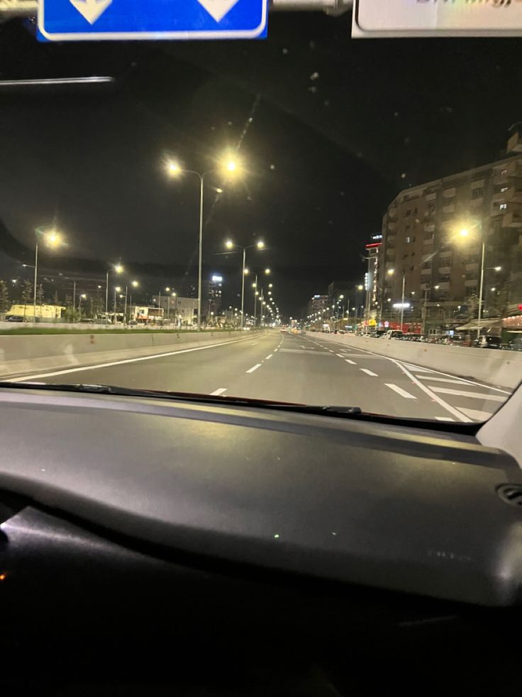 the dashboard of a car at night with street lights and buildings in the back ground