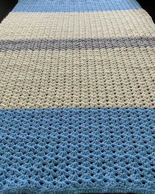 a crocheted blue and white blanket on top of a bed