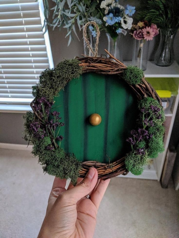 a person holding up a green door made out of twigs and grass with the words hobbit mini wreath on it