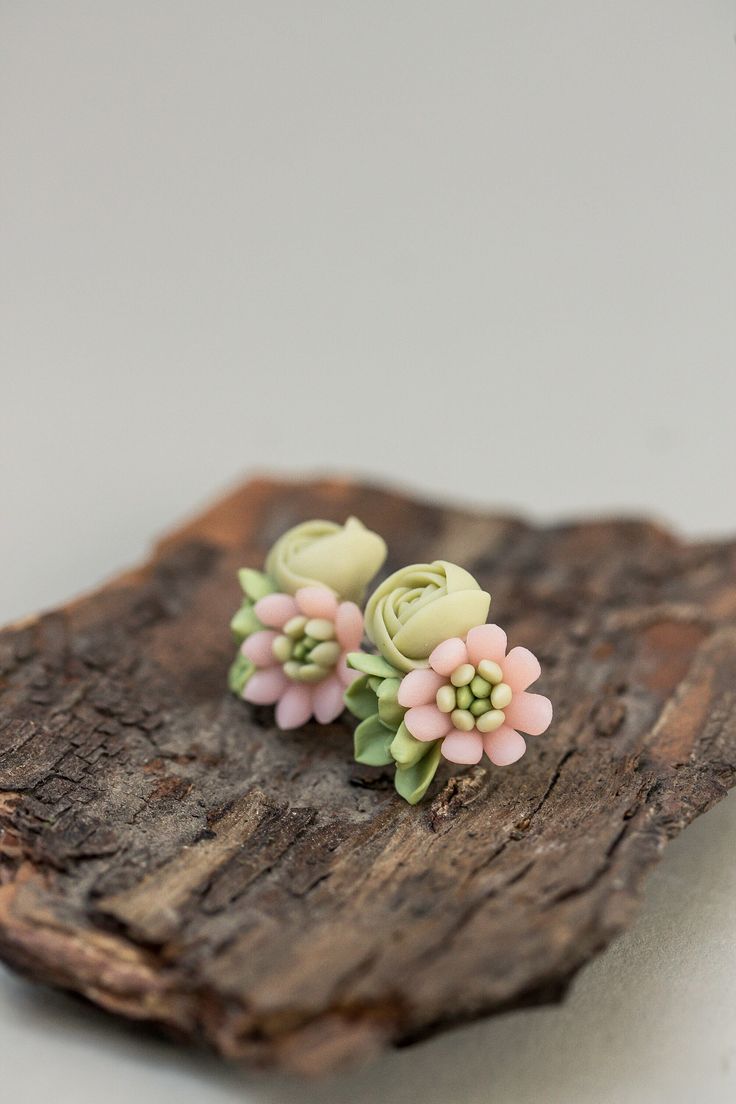 small pink and green flower earrings sitting on top of a piece of wood