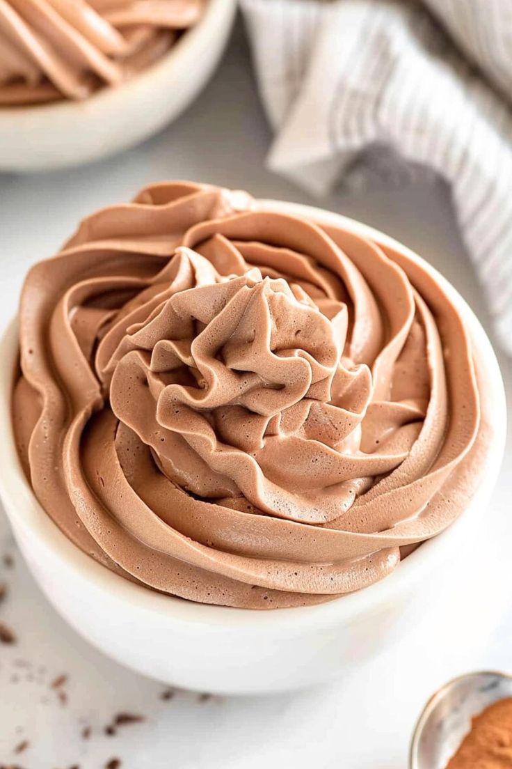 two white bowls filled with chocolate frosting on top of a table