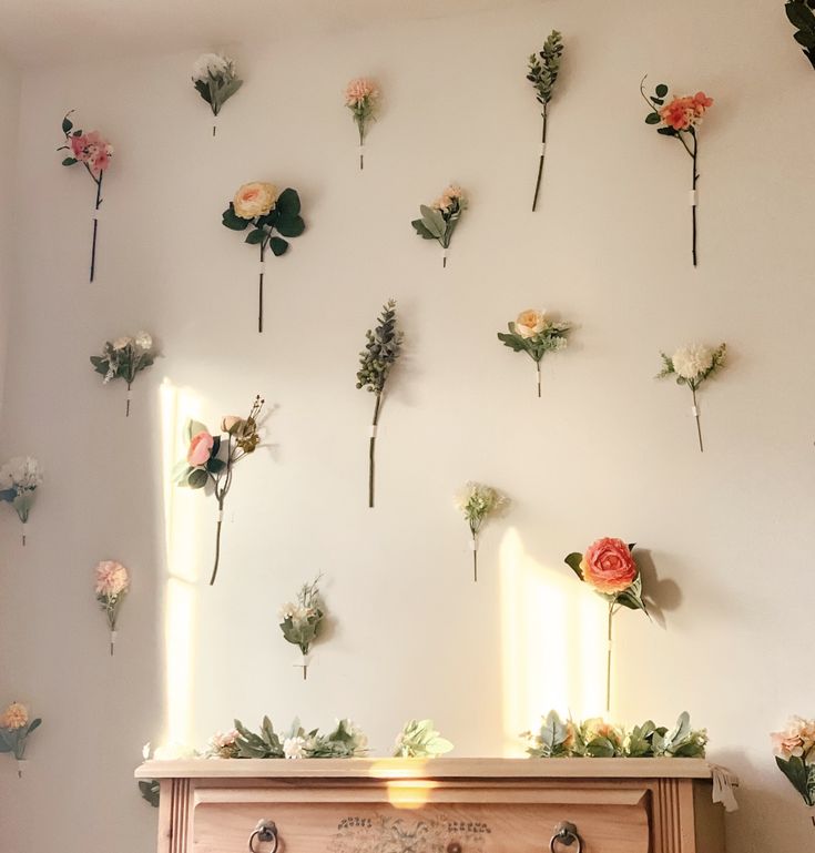 flowers are arranged on the wall above a dresser in a room with white walls and wooden drawers