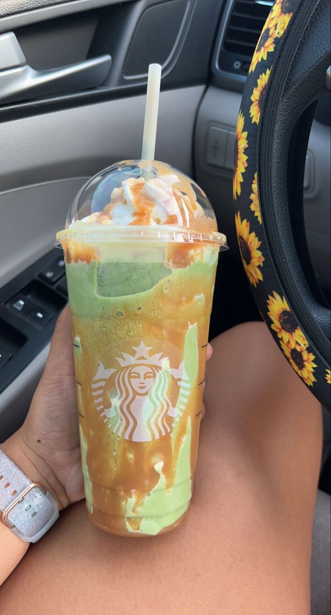 a woman holding up a starbucks drink in her hand and steering wheel behind her car