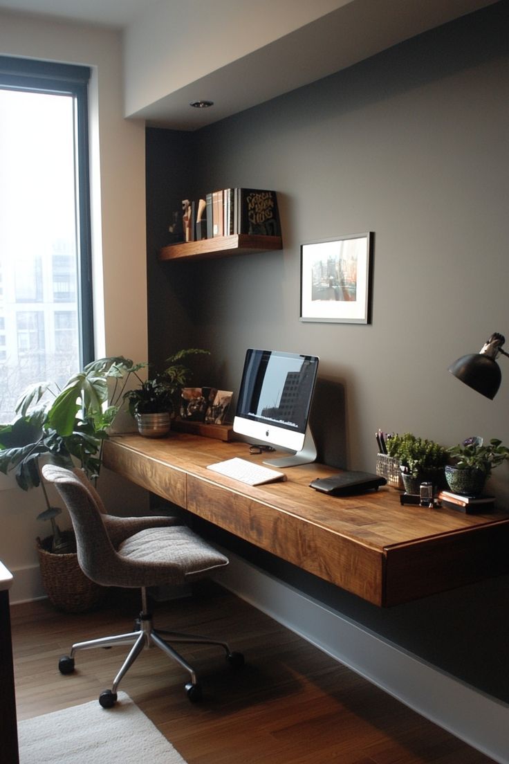 a desk with a laptop and monitor on it in front of a large window next to a potted plant