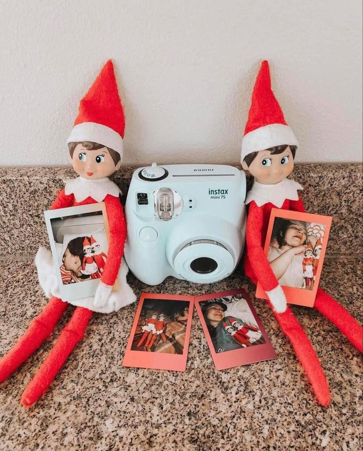 two elfs are sitting on the counter with an old camera and polaroid pictures