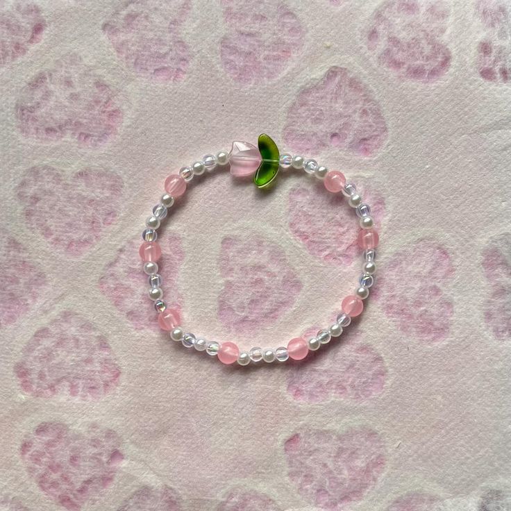 a pink and white beaded bracelet with a green leaf on it's end