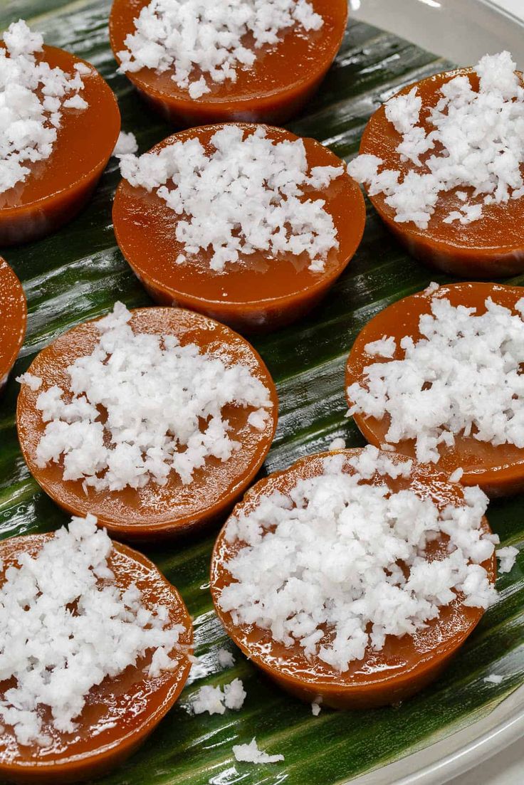 several desserts are arranged on a plate with coconut flakes around them and placed on a palm leaf