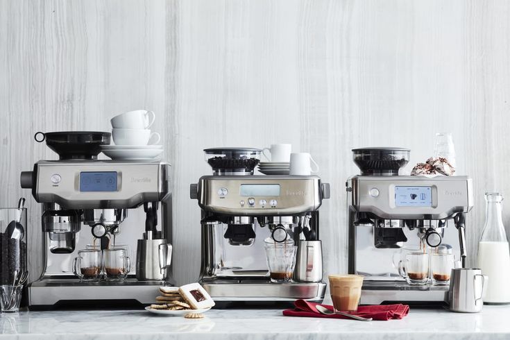 three espresso machines sitting on top of a counter next to cups and saucers