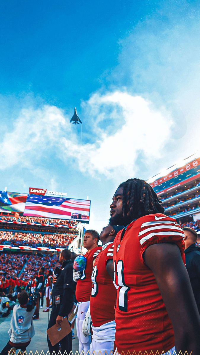 two football players are standing on the sidelines in front of an american flag and jet