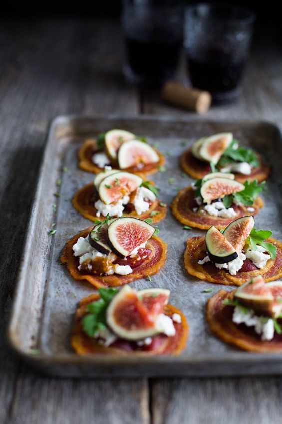 small crackers with figs, cheese and greens are on a baking sheet ready to be eaten