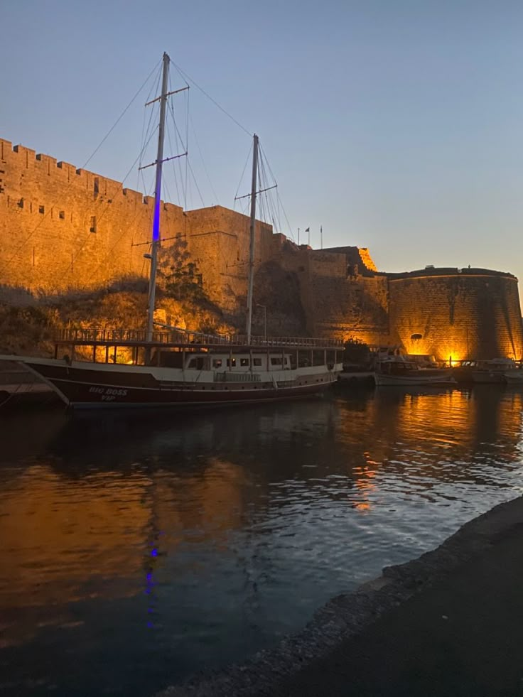 two boats are docked in the water next to an old castle at night with lights on