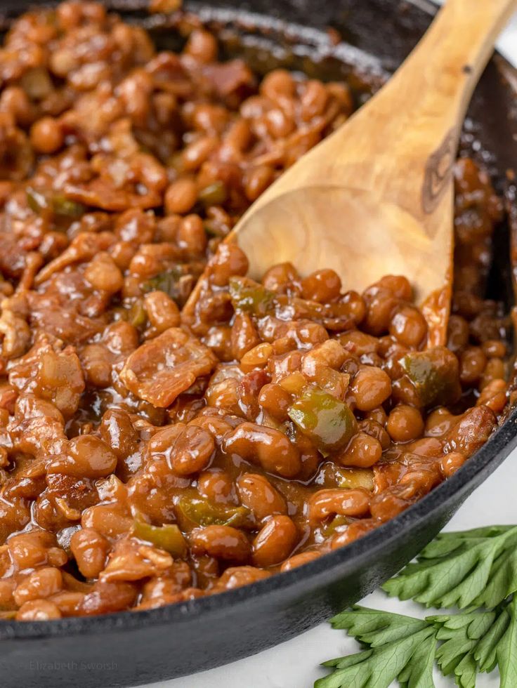 the beans are being cooked in the skillet with a wooden spoon on the side