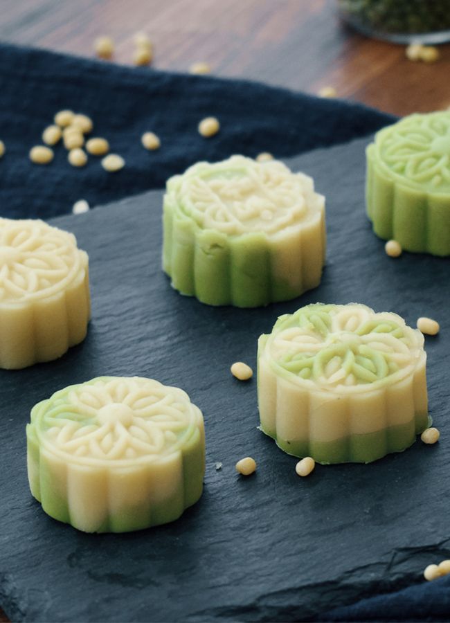 four mooncakes with green icing and white frosting on a black cloth