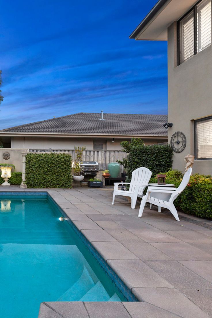 a backyard with a swimming pool and lawn chairs next to the side of the house