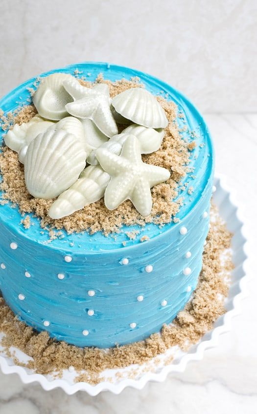 there is a blue cake decorated with sea shells and sand on the bottom, along with white polka dots